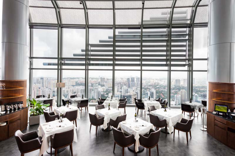 A large room in a restaurant with tables with white tablecloths, with a glass ceiling overlooking Singapore..