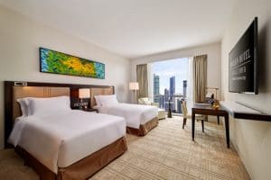 Twin beds in luxury hotel room with white ceilings, brown carpets and colourful art on wall