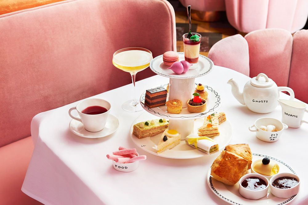Pink couches around a square white table holding colourful cakes for afternoon tea