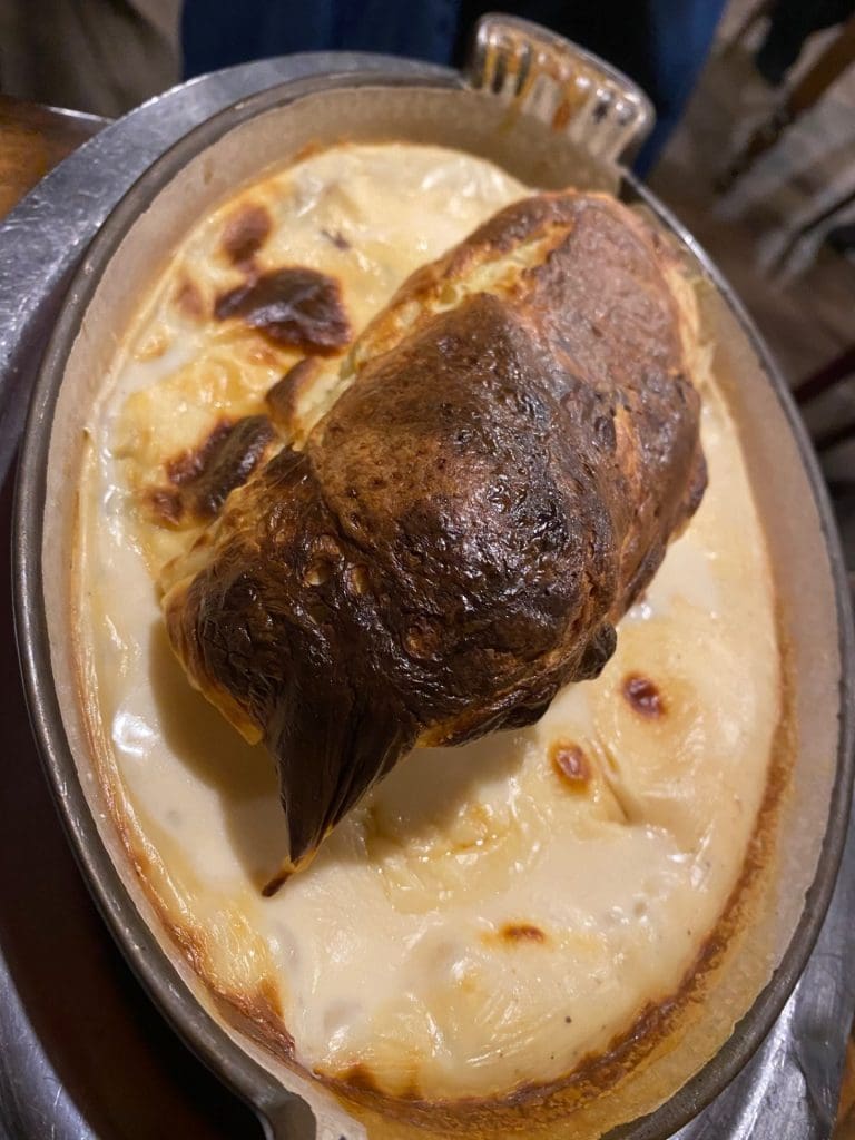 Square piece of fish topped with brown pastry in a round metal dish surrounded by a big pool of creamy pale yellow sauce