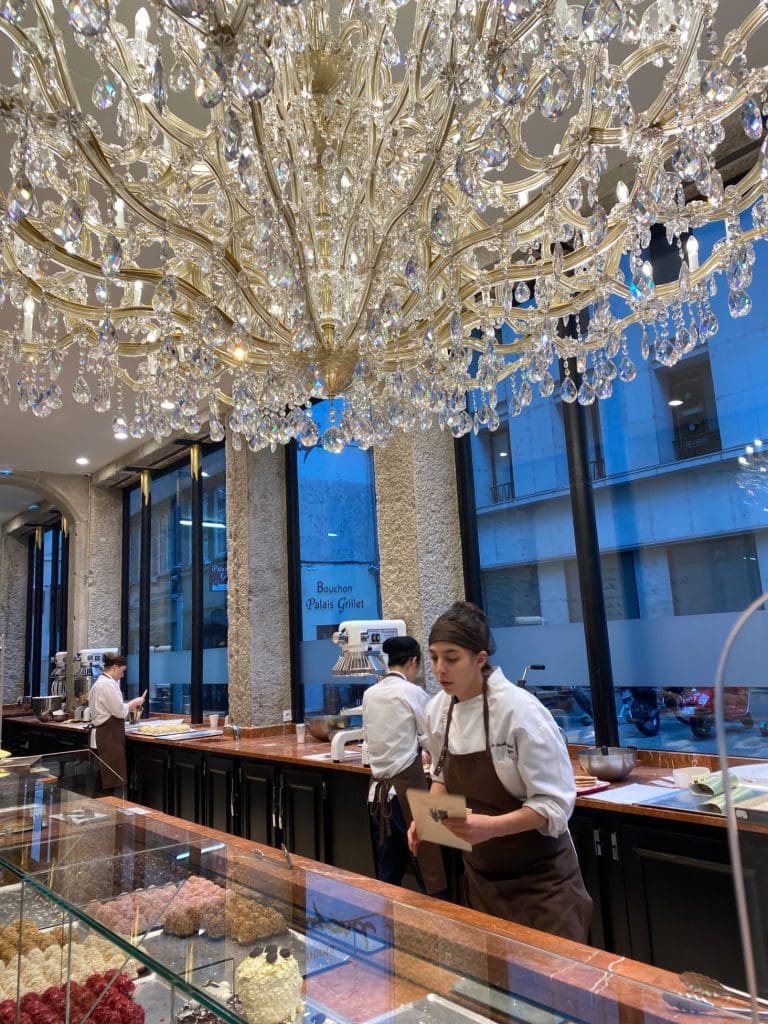 a huge crustal chandalier hanging over a glass counter with cakes.