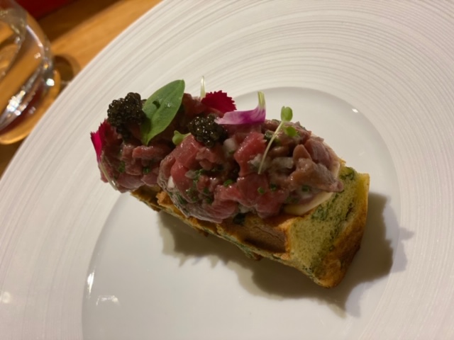 Beef tartare neatly presented on a round white plate with a savoury waffle underneath