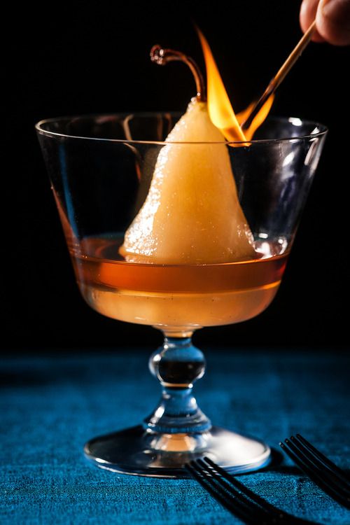 small skinless apricot coloured pear in a large gas with liquid in the bottom and a match with a flame at the top