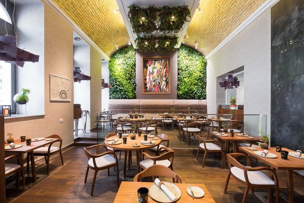 Costes restaurant budapest with a yellow ceiling, plant wall in green, and wooden tables with white later bases.