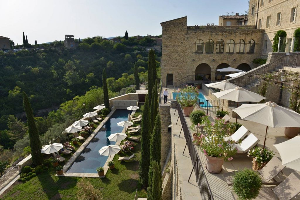 Beautiful swimming pool surrounded by white umbrellas and balcony with sun chairs in the French countryside.