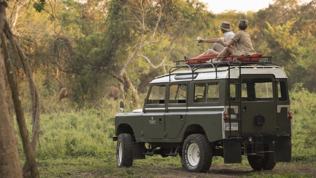 A couple on top of a land rover having a glass of wine in the jungle