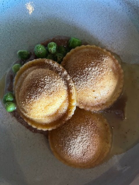 three Artisan ravioli turned up sitting on some mushrooms and green peas and the waiter poured in a Pancetta bone broth to go over it, 