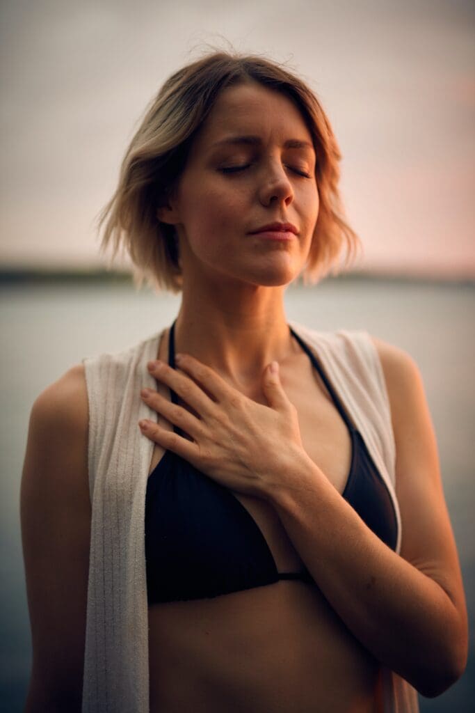Woman in white vest and black bikini with hand on chest, reflecting breathwork