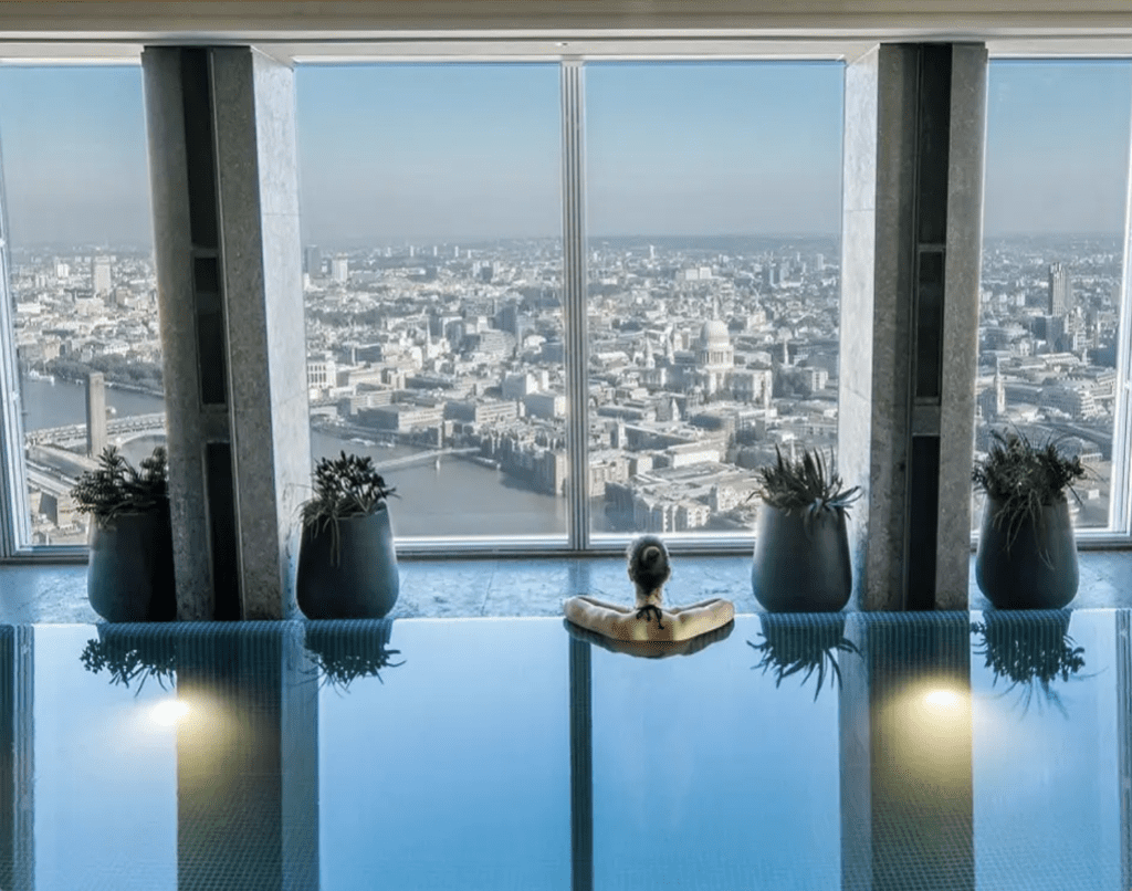 Woman in infinity pool, looking out of floor to ceiling window at London